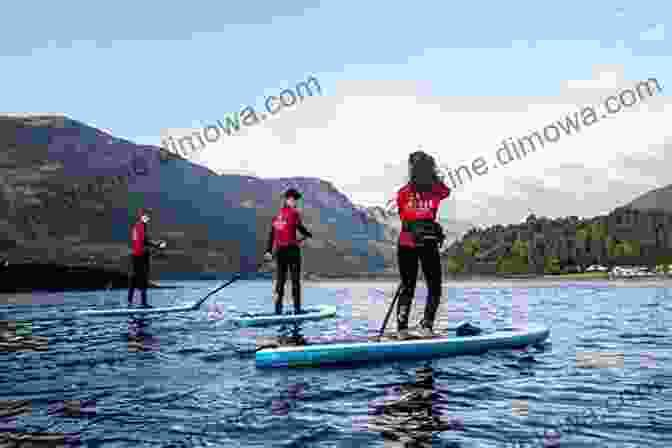 Paddleboarding On A Tranquil Scottish Loch, Surrounded By Towering Mountains And Verdant Forests Stand Up Paddleboarding In Great Britain: Beautiful Places To Paddleboard In England Scotland Wales